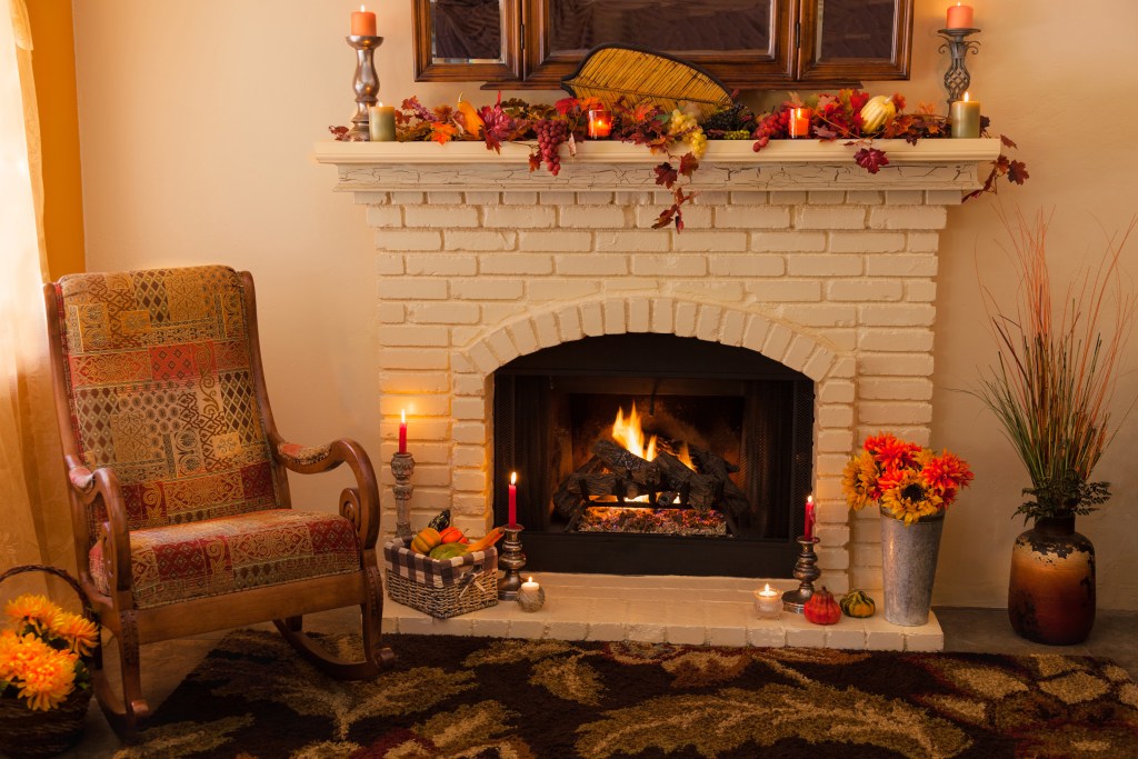 easy holiday decoration organization hacks brick fireplace has a roaring fire decorated hearth and mantel with fall Thanksgiving decor of leaves flowers pumpkins gourds candles