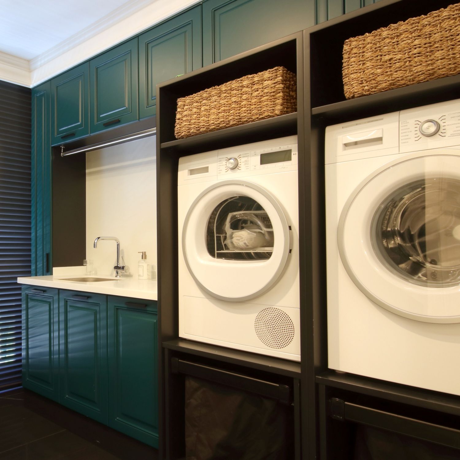 Front loading washing machines built in with extra storage in a utility room with dark green cabinets and white counter with sink.