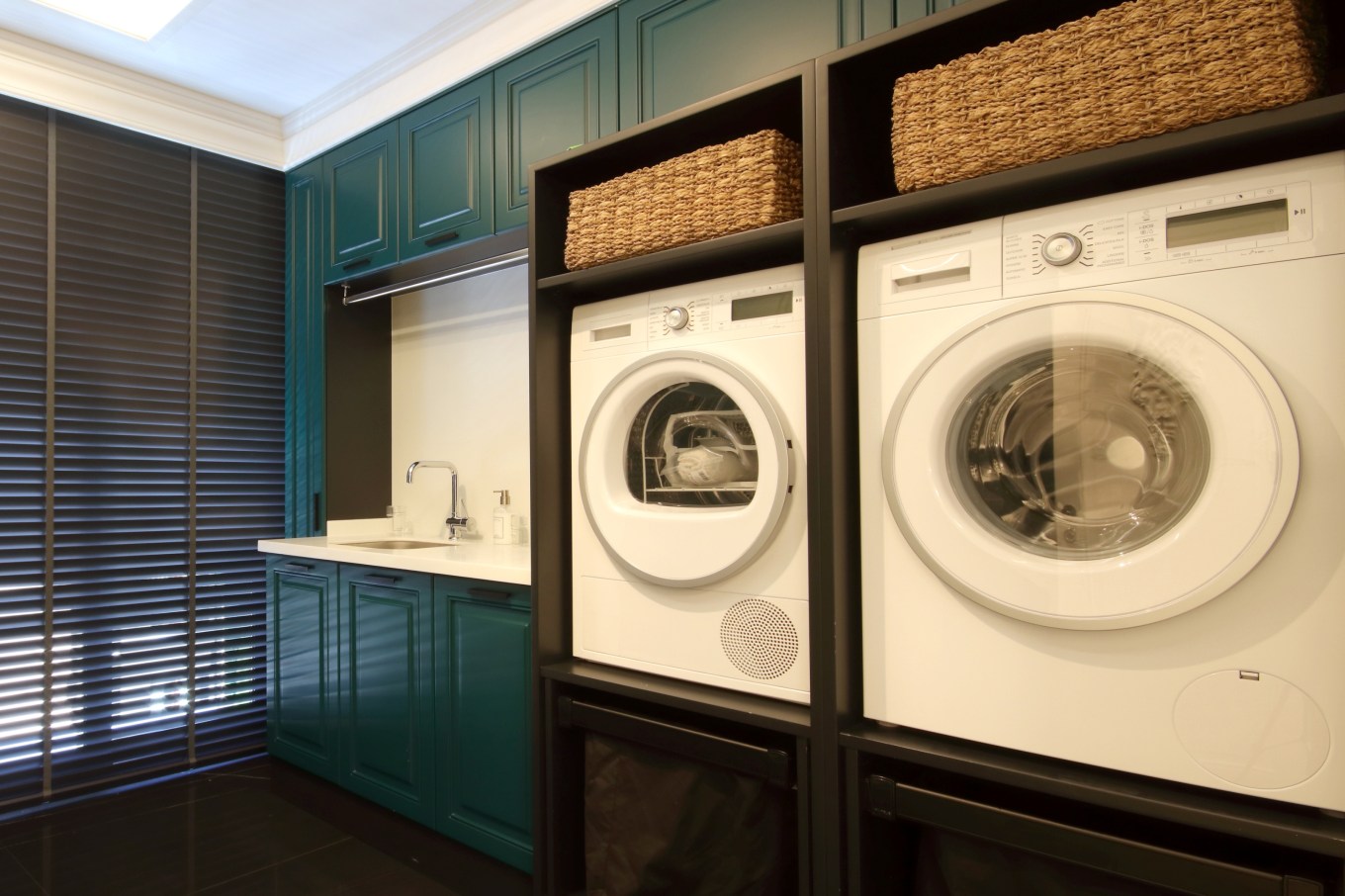 Front loading washing machines built in with extra storage in a utility room with dark green cabinets and white counter with sink.