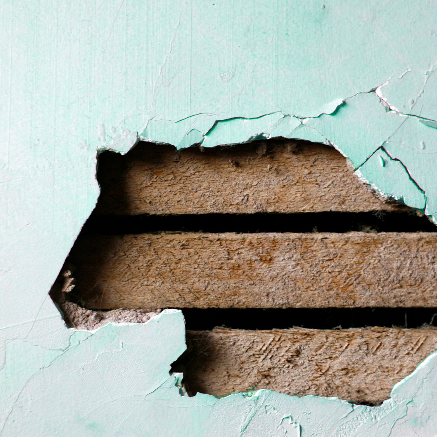 closeup of a hole in a plaster wall with exposed wood lath