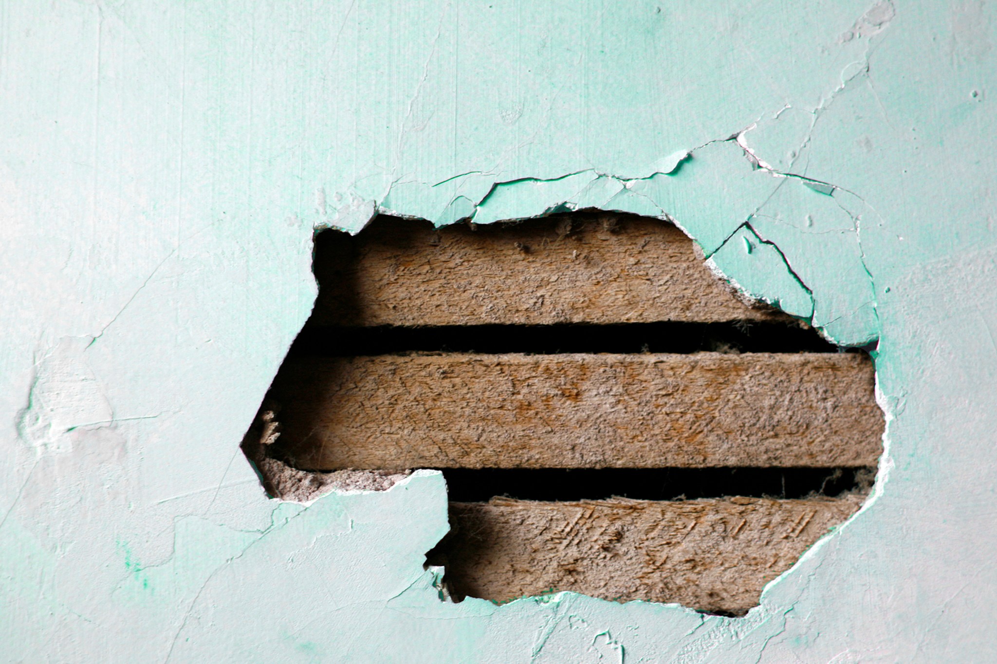 closeup of a hole in a plaster wall with exposed wood lath