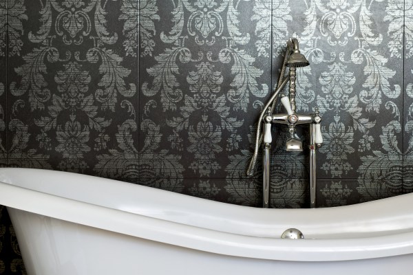 white clawfoot tub with a vintage looking brushed silver faucet and handheld shower head in front of a fancy floral dark and light gray wallpaper