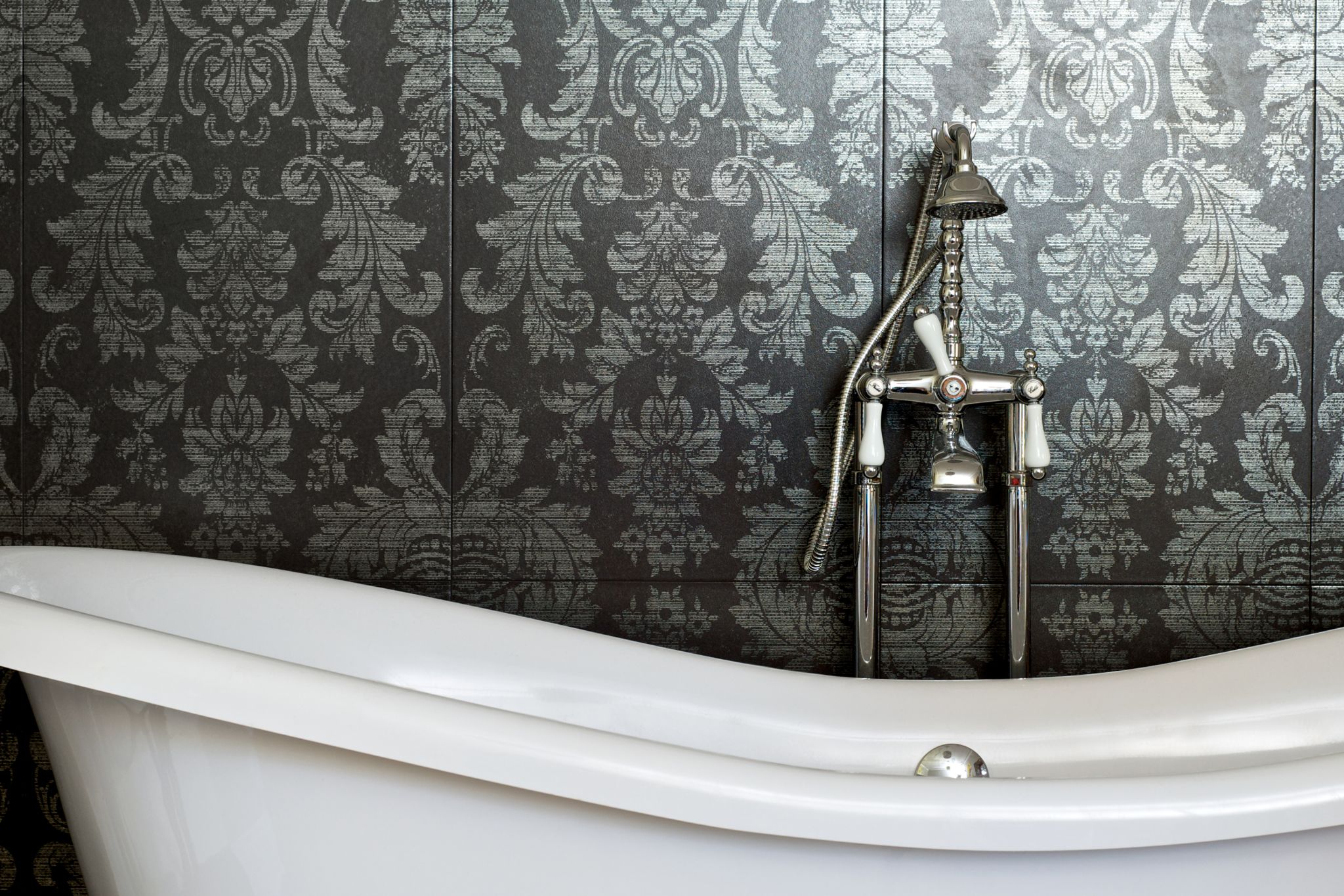 white clawfoot tub with a vintage looking brushed silver faucet and handheld shower head in front of a fancy floral dark and light gray wallpaper