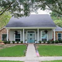 front view of renovated Acadian style home with painted and brick exterior and colorful front door with columns and tall trees in the yard