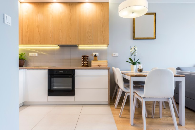 modern kitchen interior with wood upper cabinets and white lower cabinets the floor has large white tiles and wood planks under a wooden dining table next to a gray couch