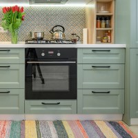 modern kitchen with light green cabinets and white countertop decorated with flowers and cooking utensils and colorful patterned backsplash with a gas cooktop and black oven