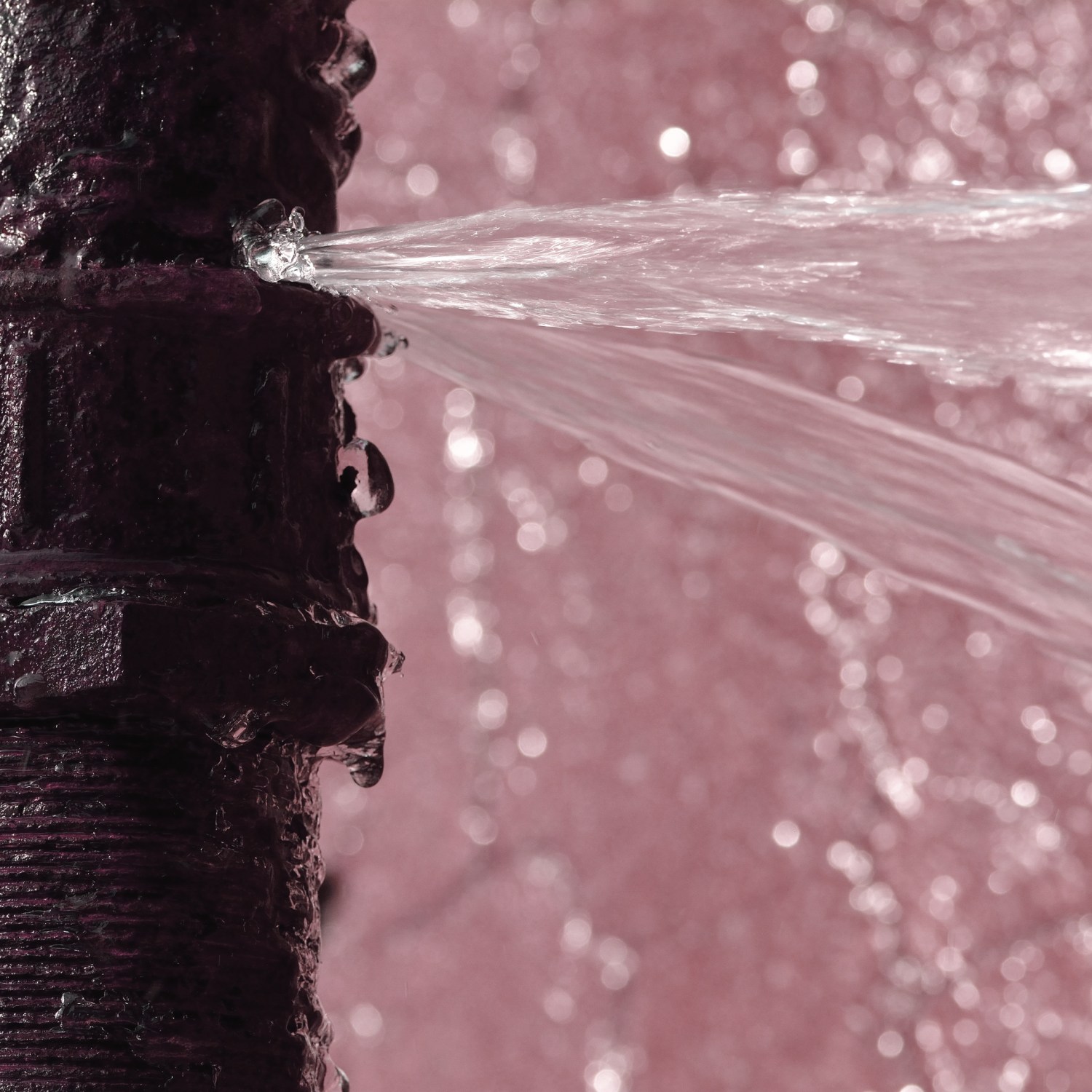 an old rusty pipe burst with water spewing out with a light pinkish purple background