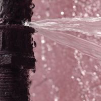 an old rusty pipe burst with water spewing out with a light pinkish purple background