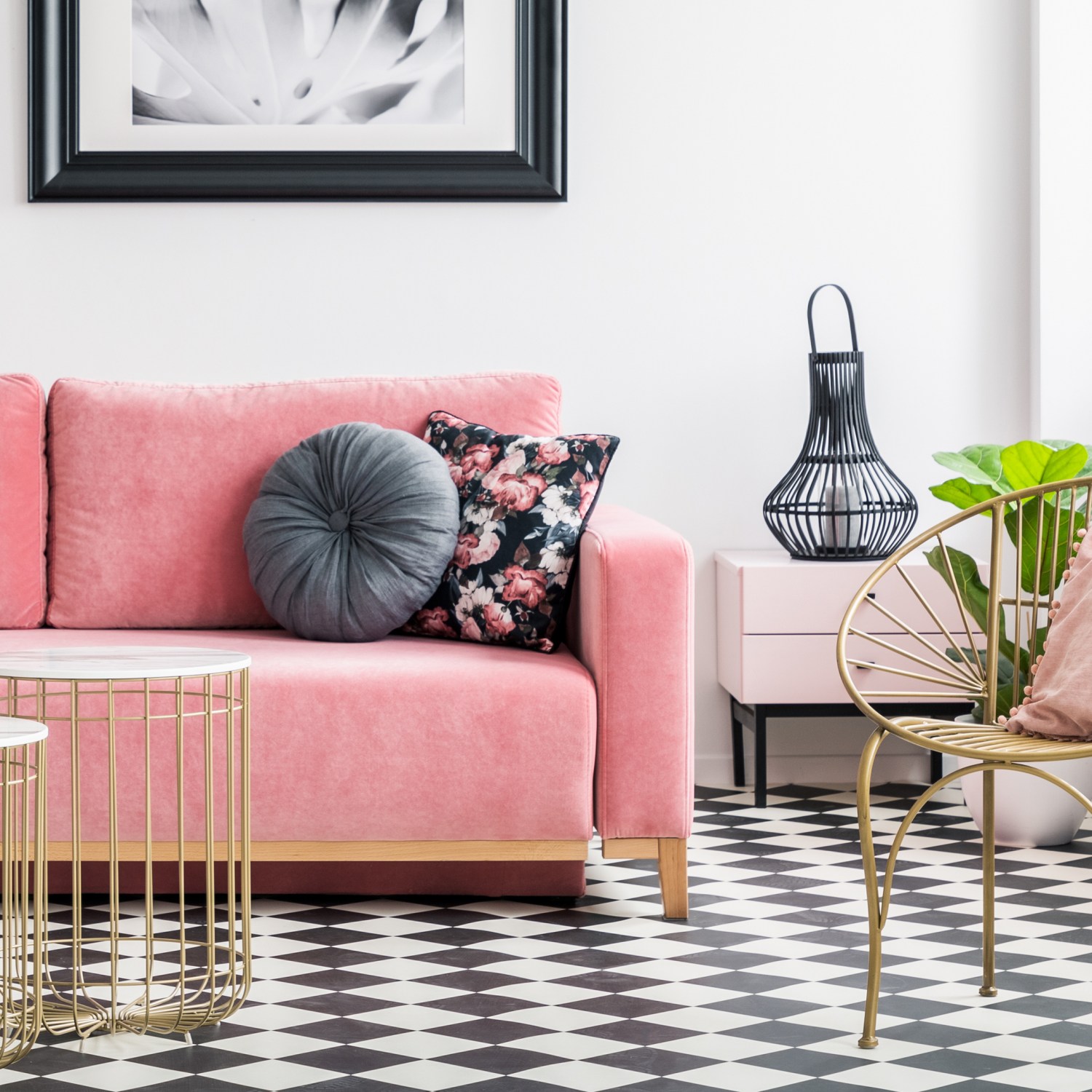photo of a living room interior with a pink velvet sofa golden armchair and tables with decorative lights and plants with a wall painting and checkered tile floor