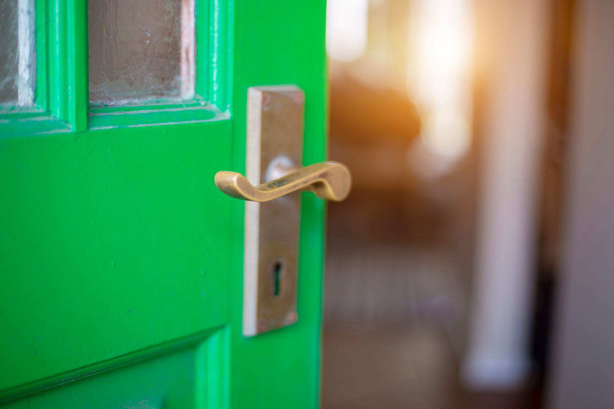 ajar vintage green door with small window panes with brass handle and skeleton key hole