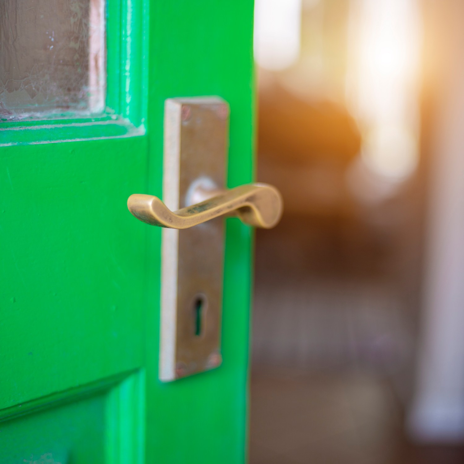 ajar vintage green door with small window panes with brass handle and skeleton key hole