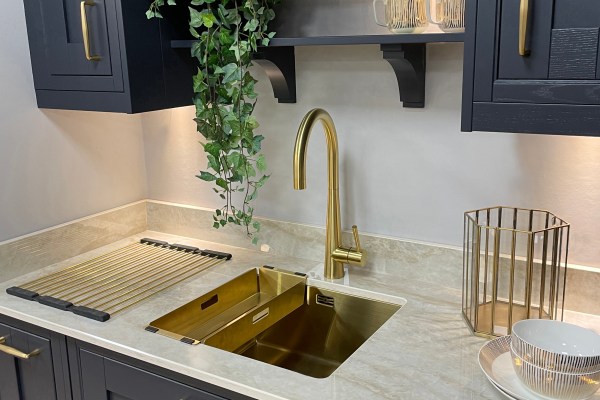 image of gold sink with gold single lever tap inset in a white marble kitchen counter with upper and lower navy wood cabinets with gold hardware