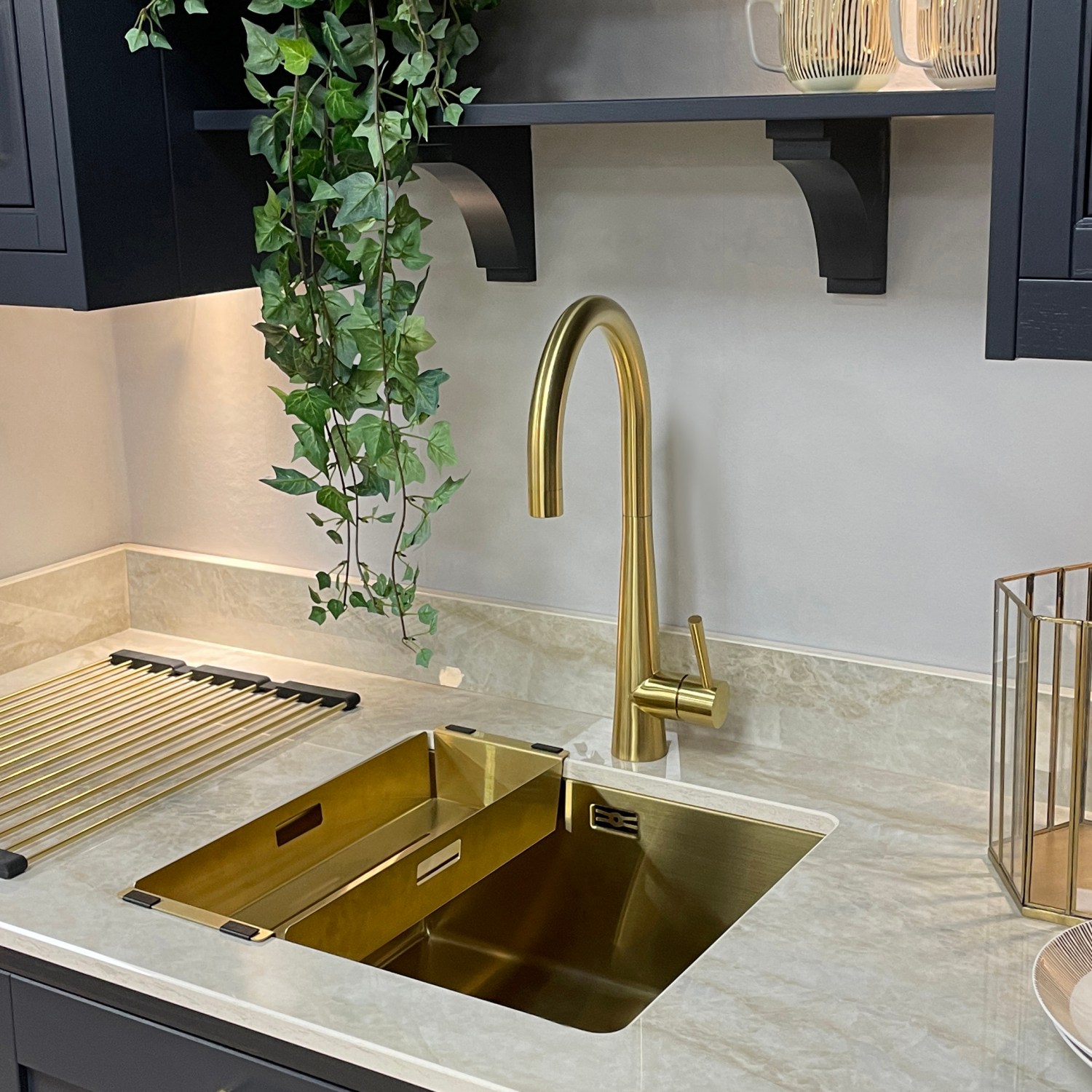 image of gold sink with gold single lever tap inset in a white marble kitchen counter with upper and lower navy wood cabinets with gold hardware