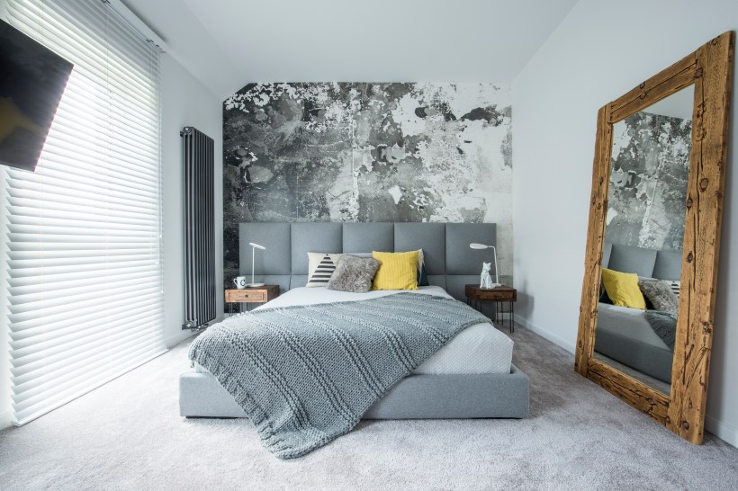 gray blanket on gray bed with yellow pillow in updated bedroom interior with large wood framed mirror