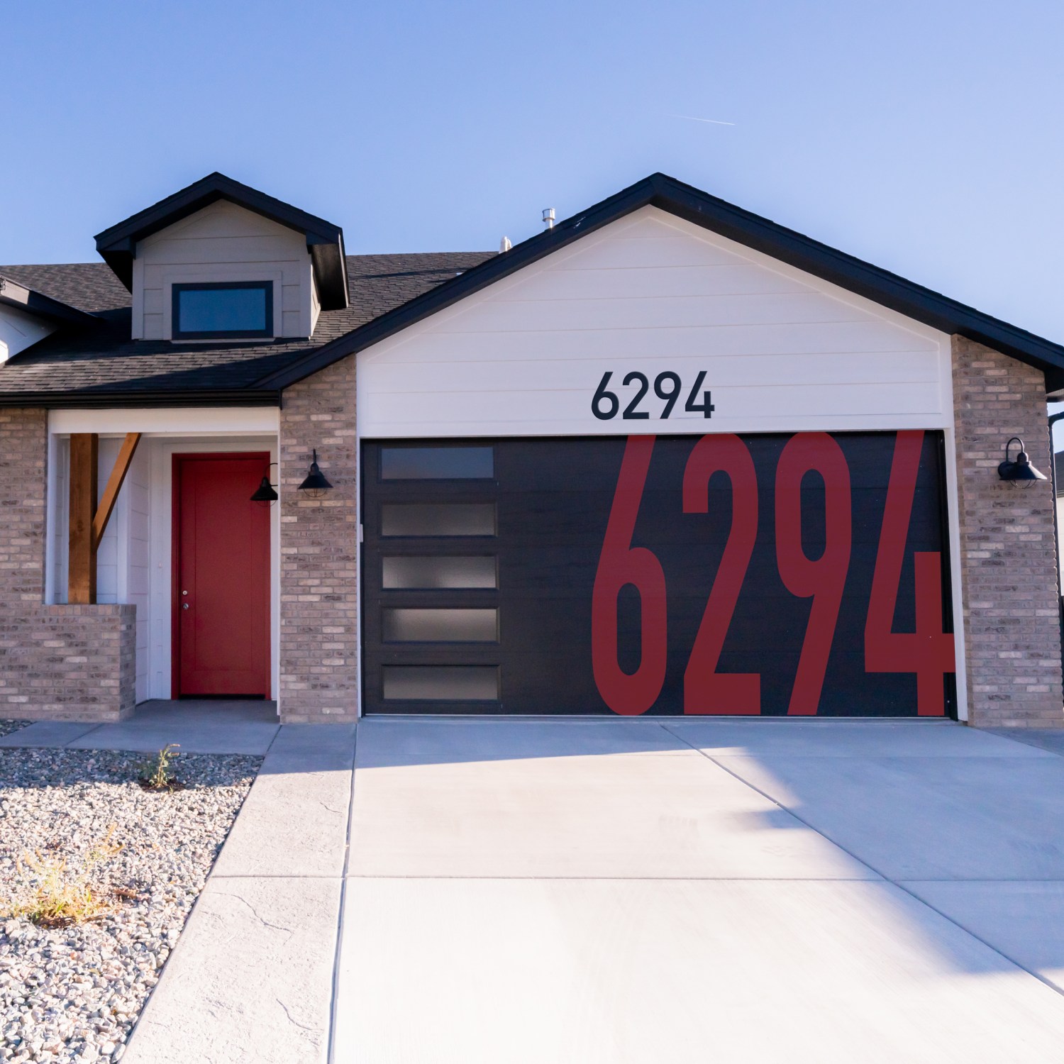 front exterior trendy home with brick and white siding has large red house numbers painted on black garage door