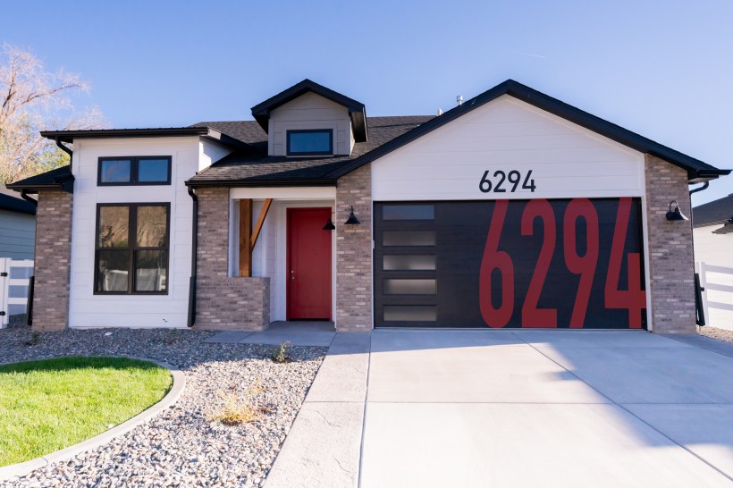 front exterior trendy home with brick and white siding has large red house numbers painted on black garage door