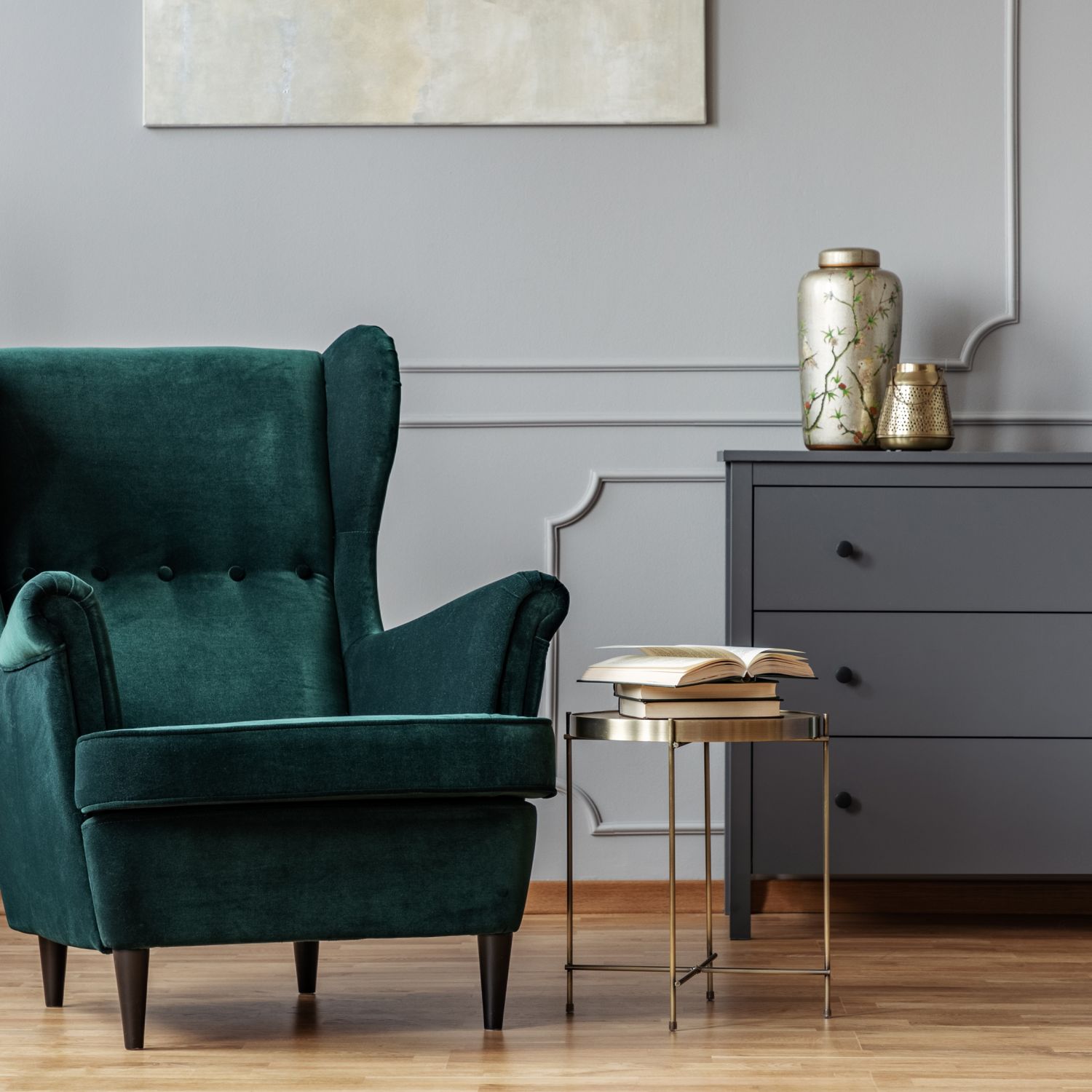 trendy home design of small golden table next to green velvet wing back chair in gray living room