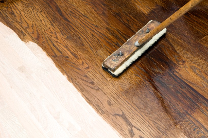 almost finished dark stain application with handheld pole and pad on new oak hardwood floor