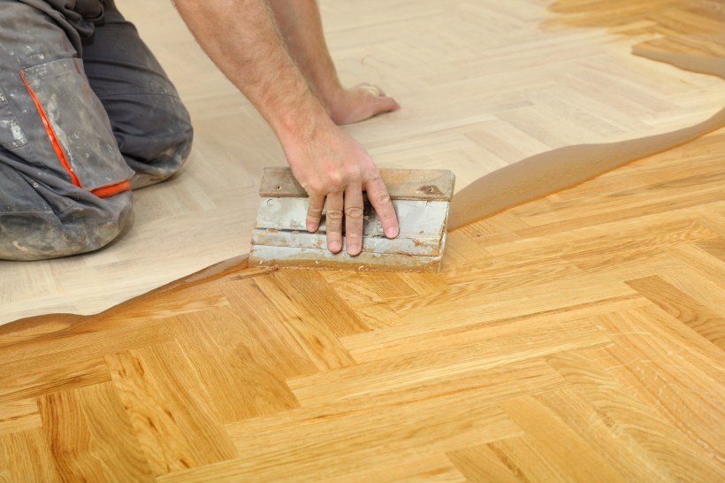 hardwood flooring installation workers hand and tool varnishing of oak parquet herringbone floor light warm color