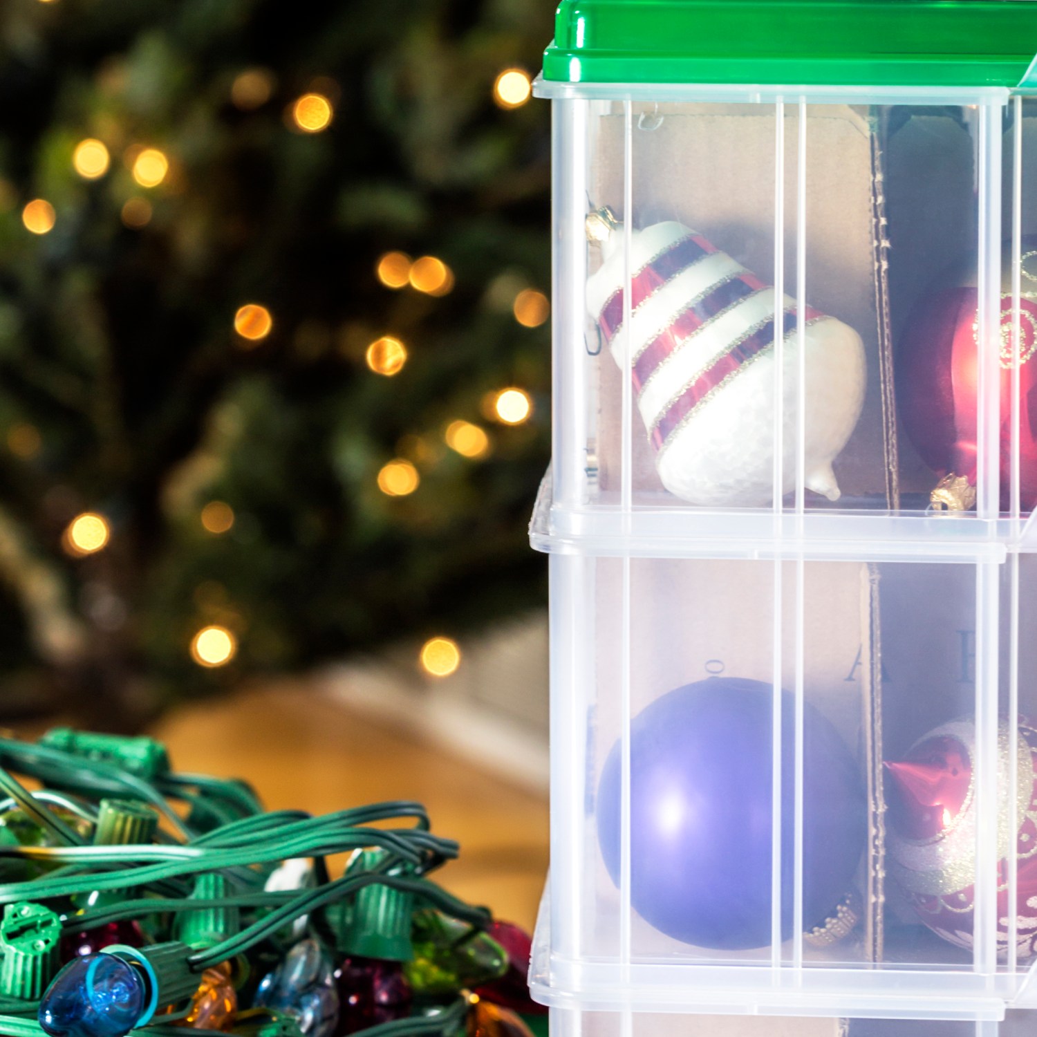 organized holiday decor lights and ornaments in clear storage bins with blurred christmas tree in background