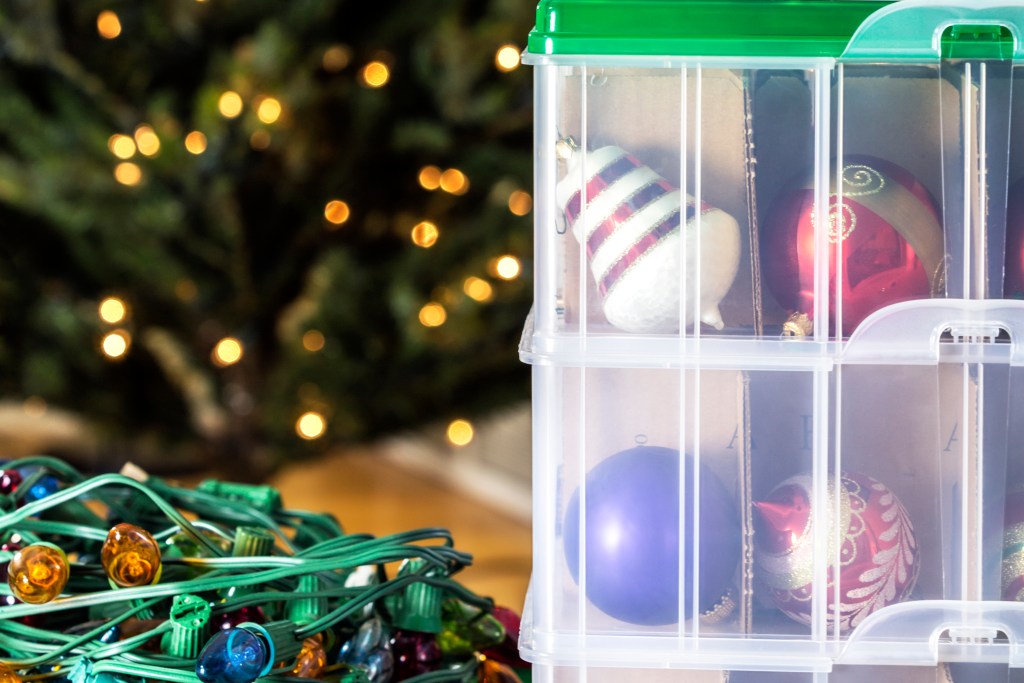 organized holiday decor lights and ornaments in clear storage bins with blurred christmas tree in background