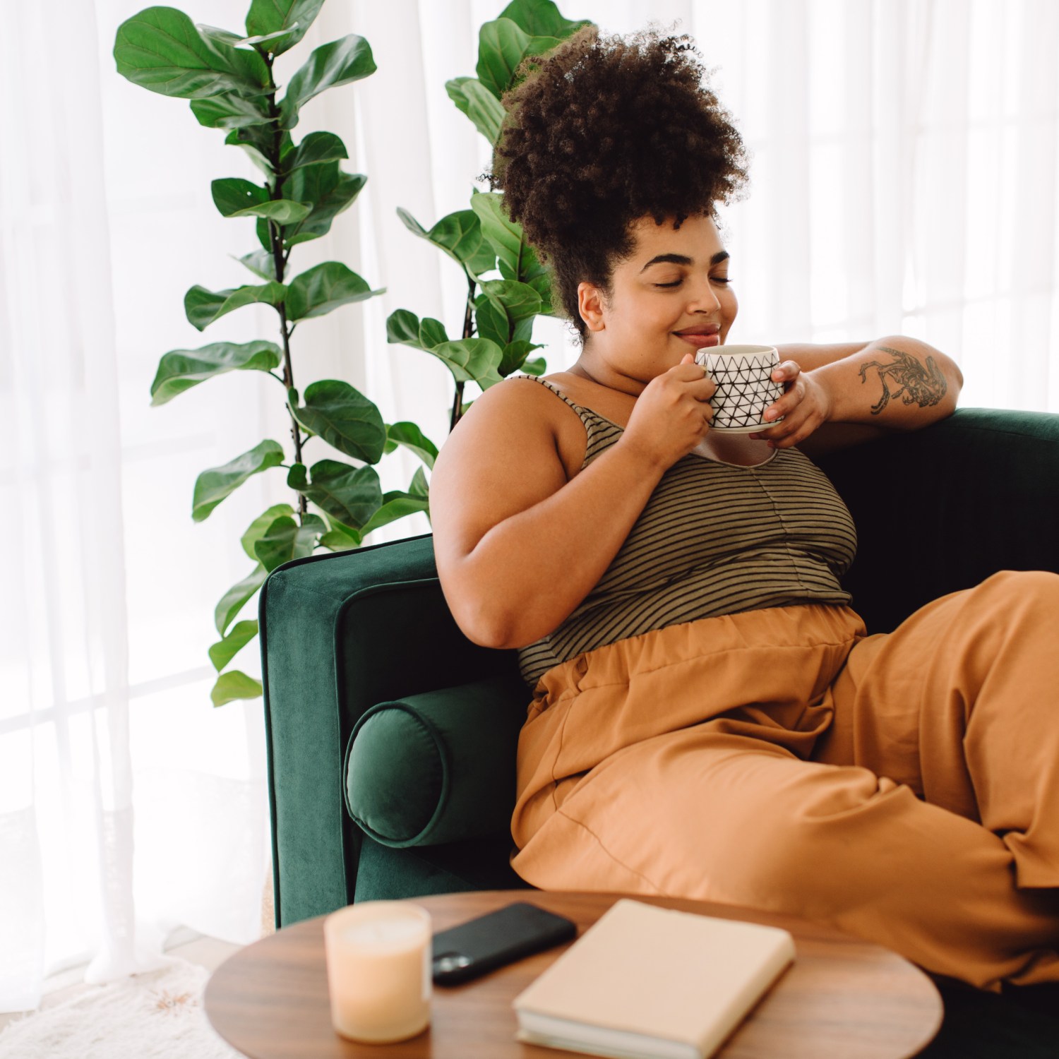 a beautiful woman at home relaxing on a green sofa holding a cup of coffee