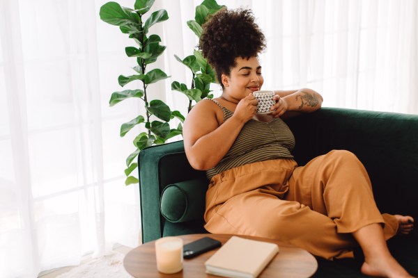 a beautiful woman at home relaxing on a green sofa holding a cup of coffee