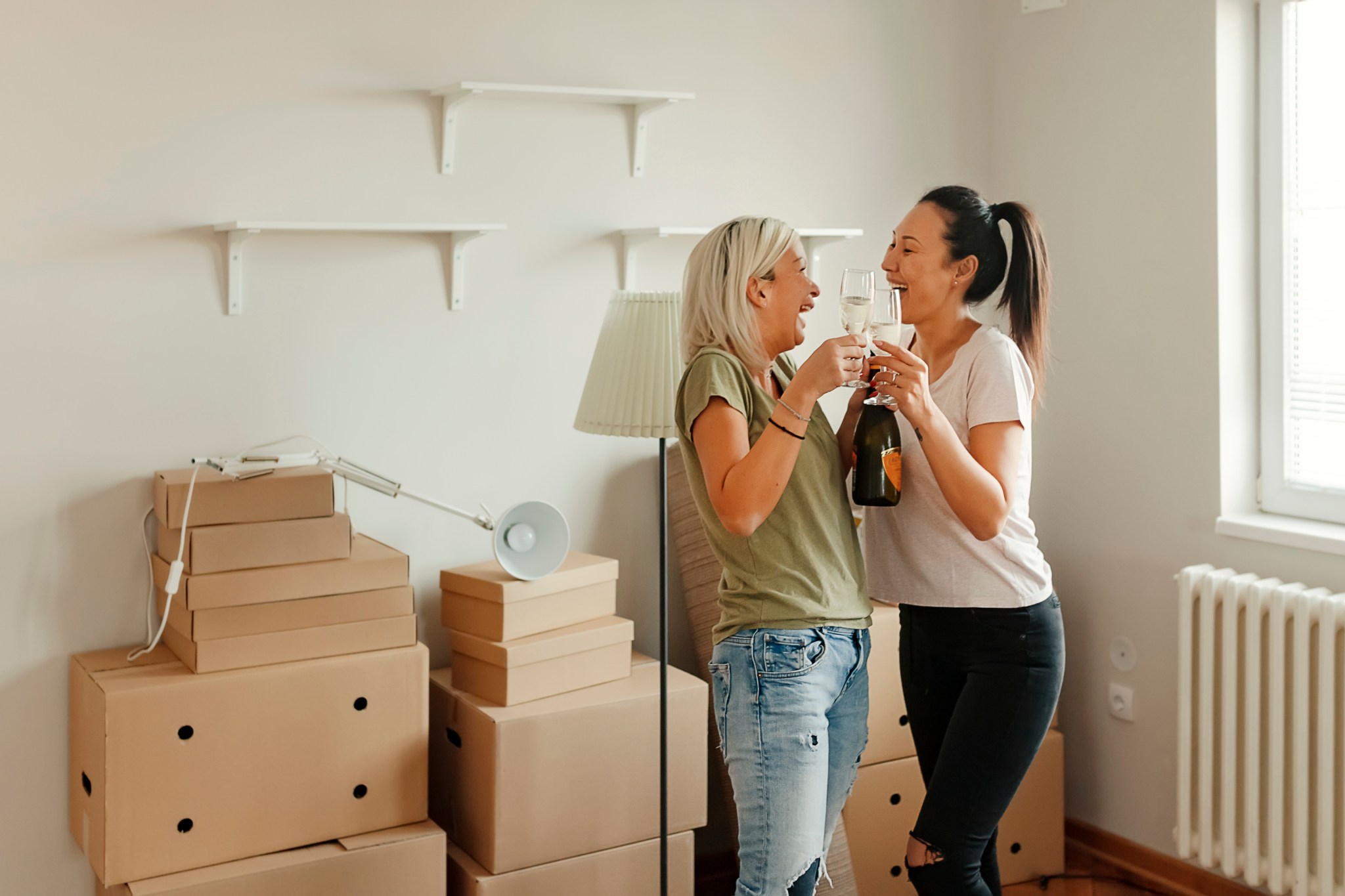 two female first time home buyers celebrate new house purchase ownership on moving day standing among boxes