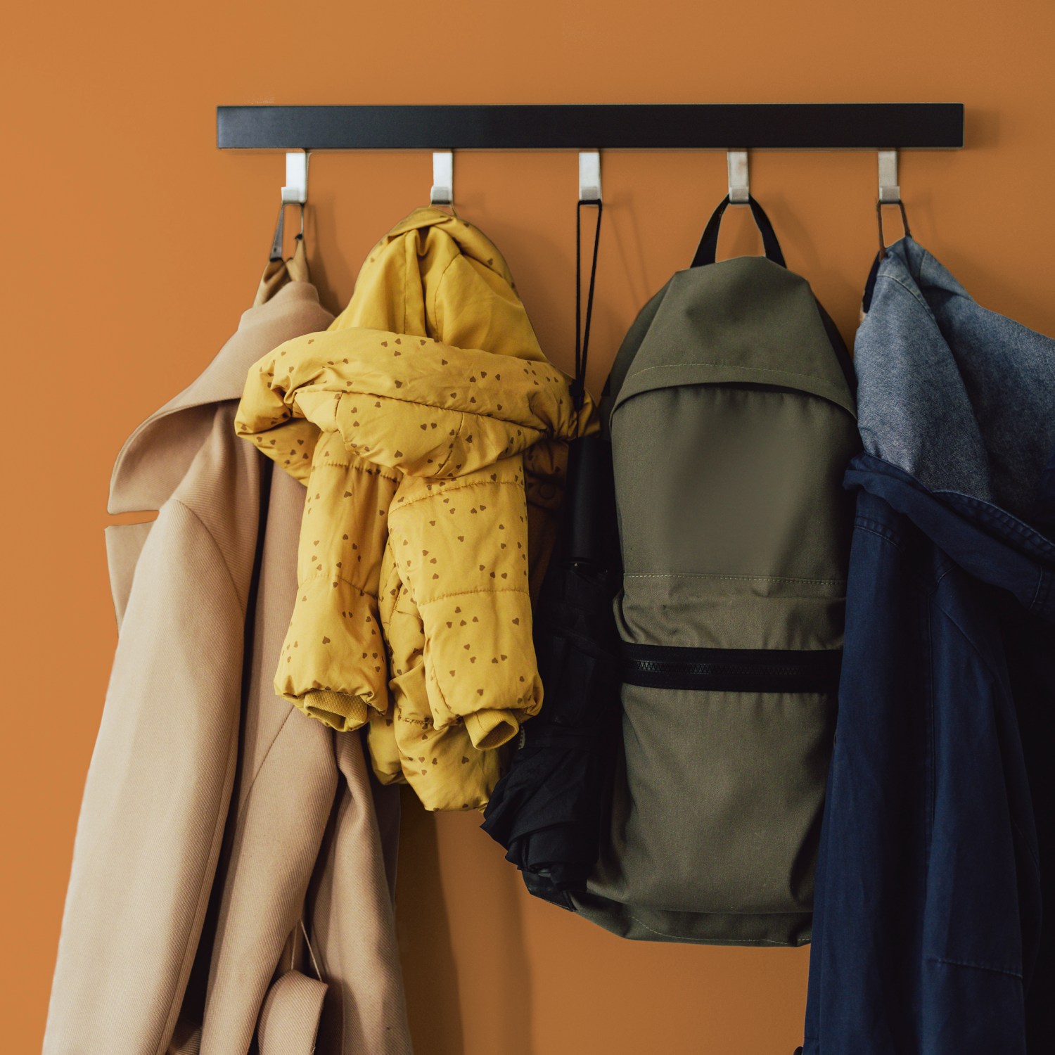 organized coatrack with three jackets and a backpack hanging on coathook on orange wall in a decluttered home