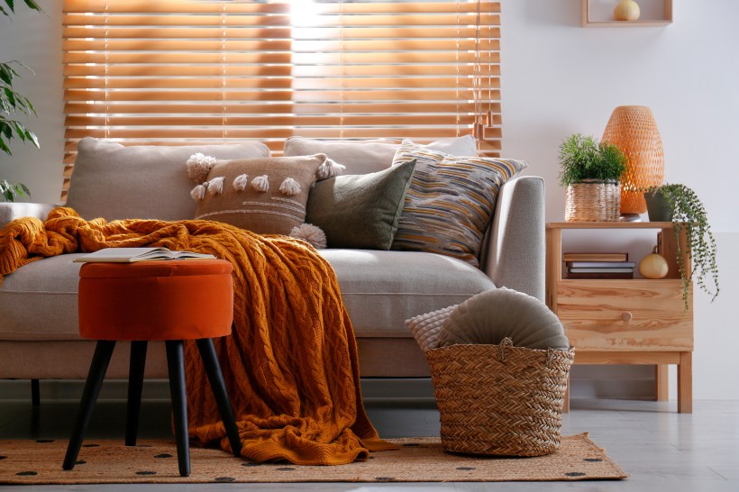 decluttered home neutral living room interior with comfy sofa, orange blanket and ottoman, organized side table storage