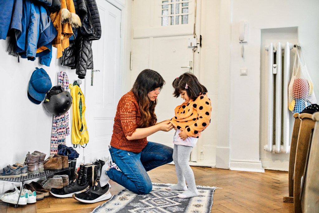 mother helping young girl put on jacket in mudroom entryway of home