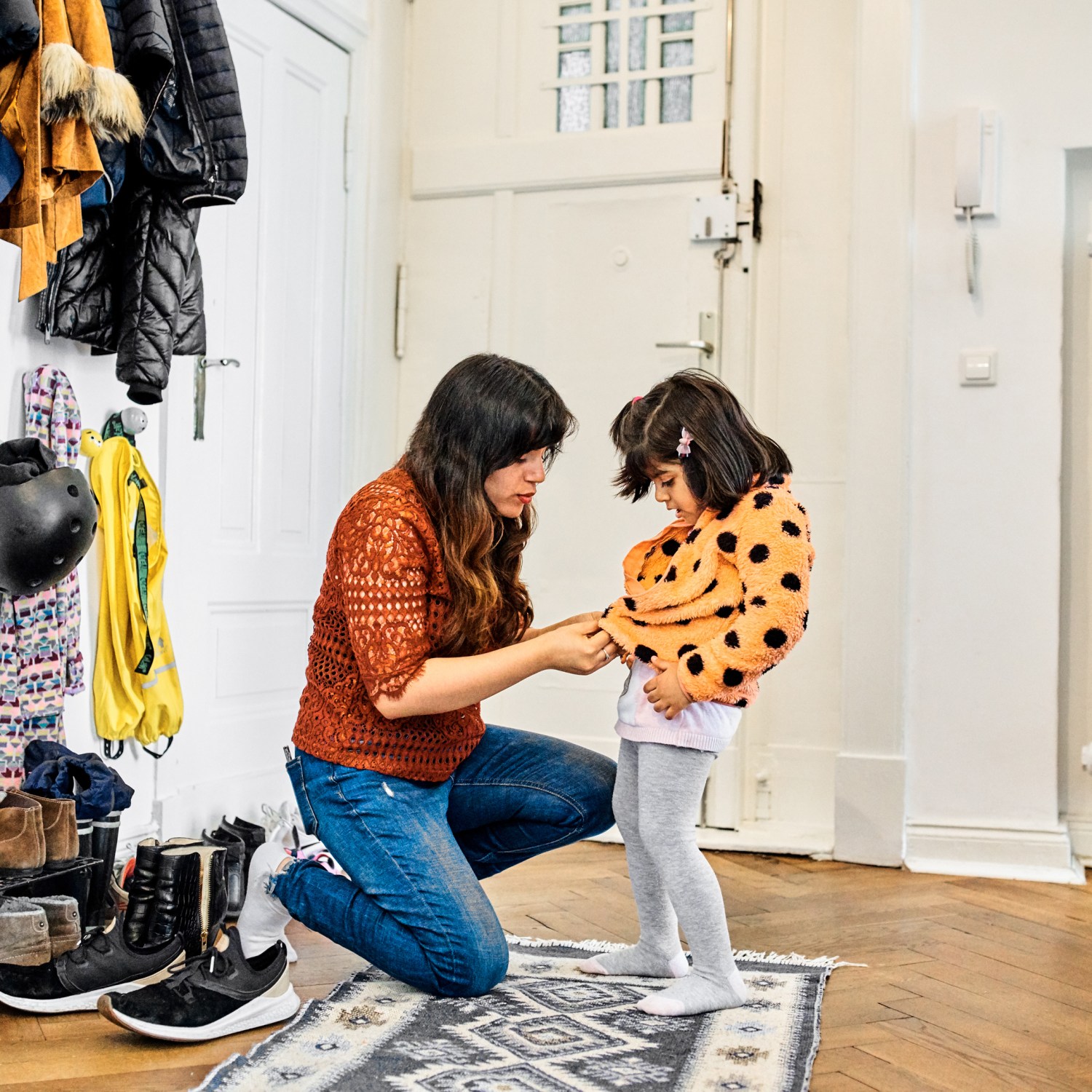 mother helping young girl put on jacket in mudroom entryway of home