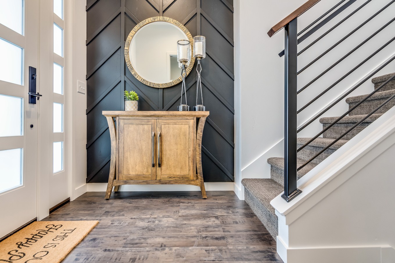 foyer of home with wood console table gold mirror against gray wall and modern white front door of entryway