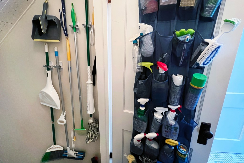 home cleaning products organized in hallway to basement shoe caddy on door broom mops dusters hang on wall
