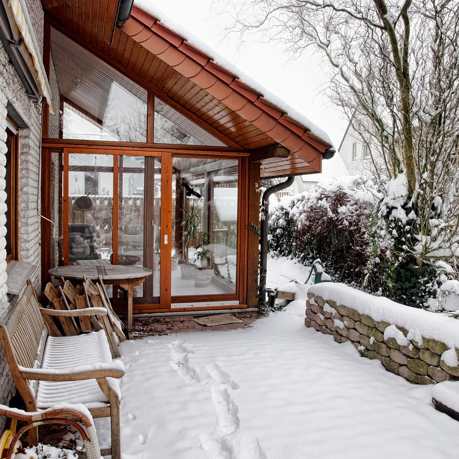 terrace of a home with large light windows covered in snow on a bright winter day