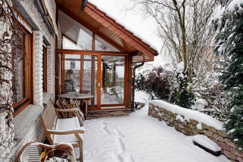 terrace of a home with large light windows covered in snow on a bright winter day