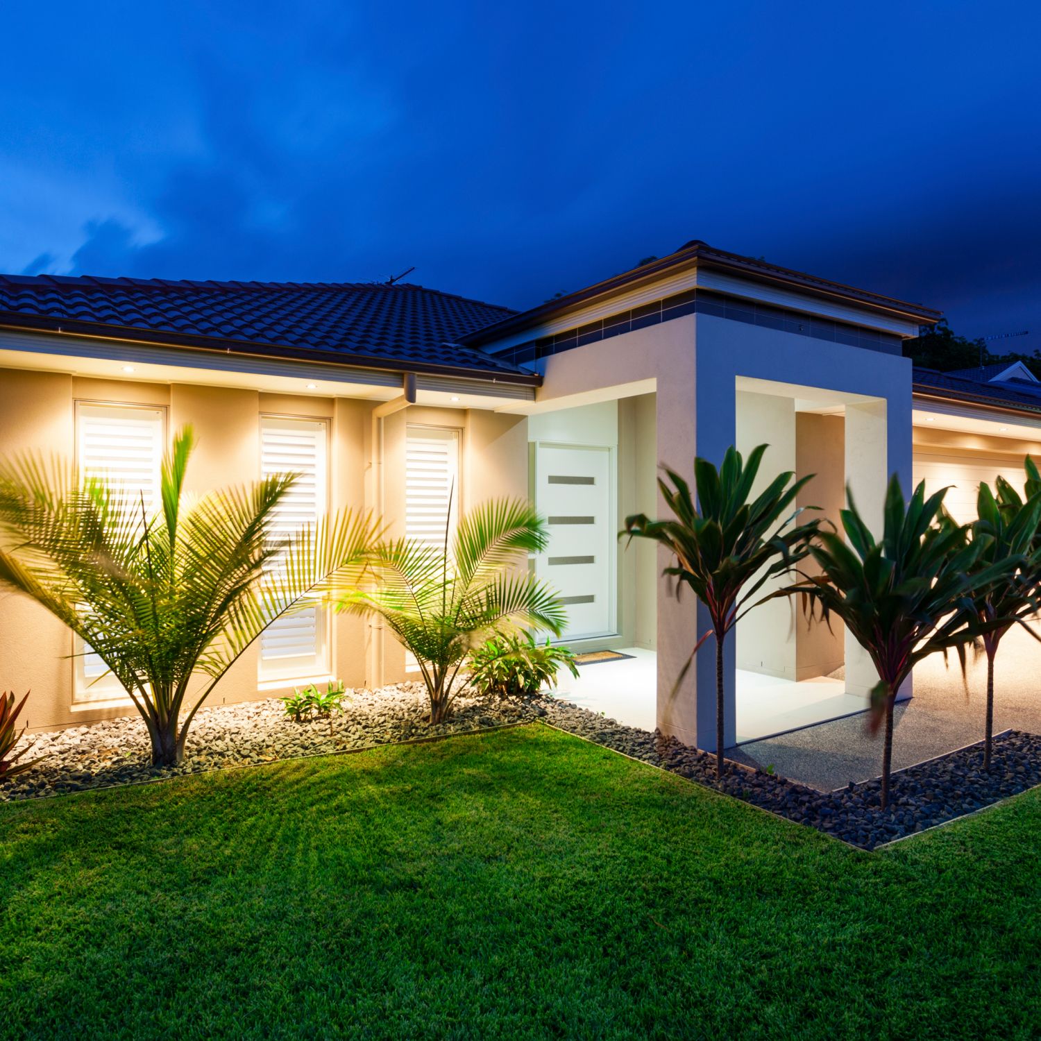 outdoor exterior lighting at dusk of modern white house gives inviting glow of home and landscaping