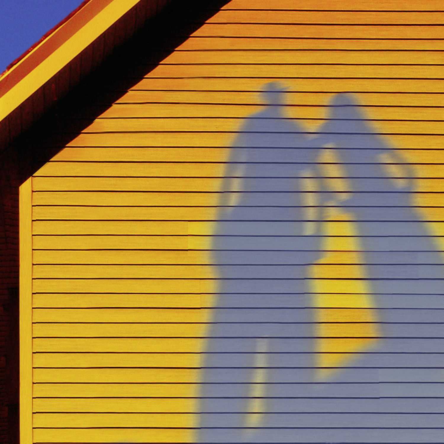 Shadows of two people on the clean yellow siding of a home with a bright blue sky in the background