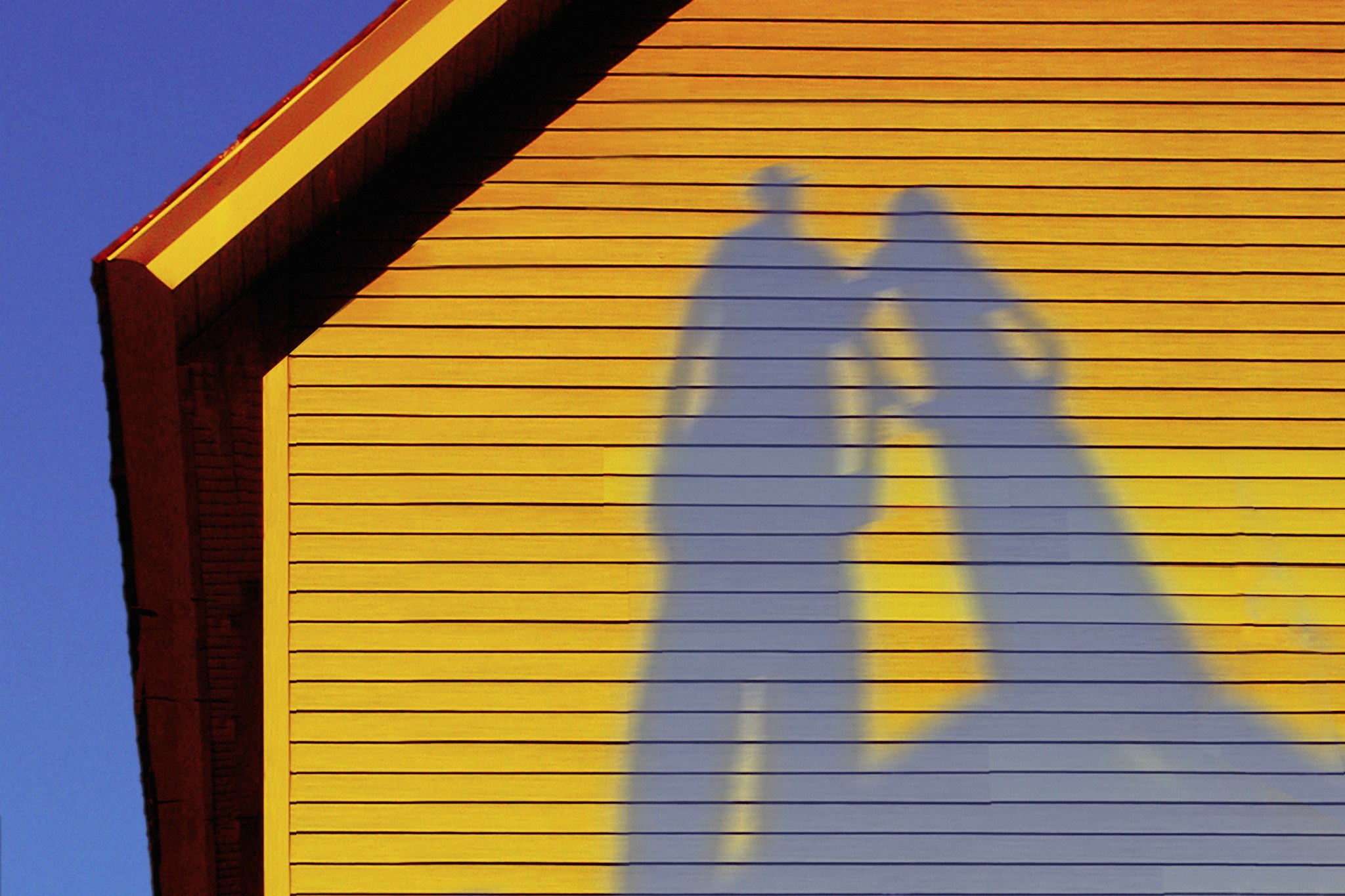 Shadows of two people on the clean yellow siding of a home with a bright blue sky in the background