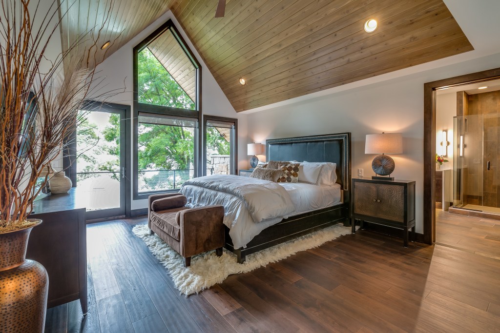 primary suite idea has wall of windows natural wood floor cathedral ceiling spacious bedroom and bath layout
