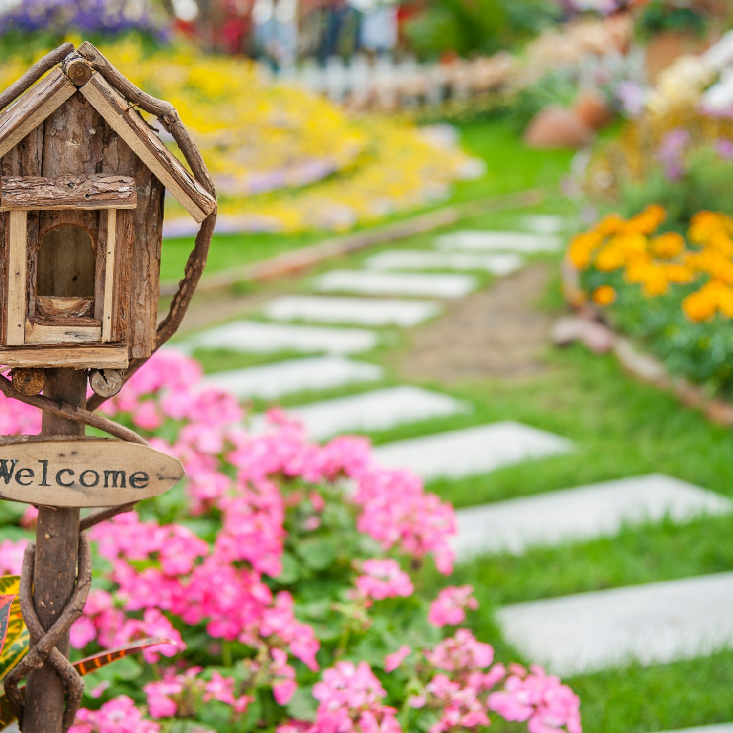 welcome yard sign on a small birdhouse in colorful landscaped garden in maintained yard of a home