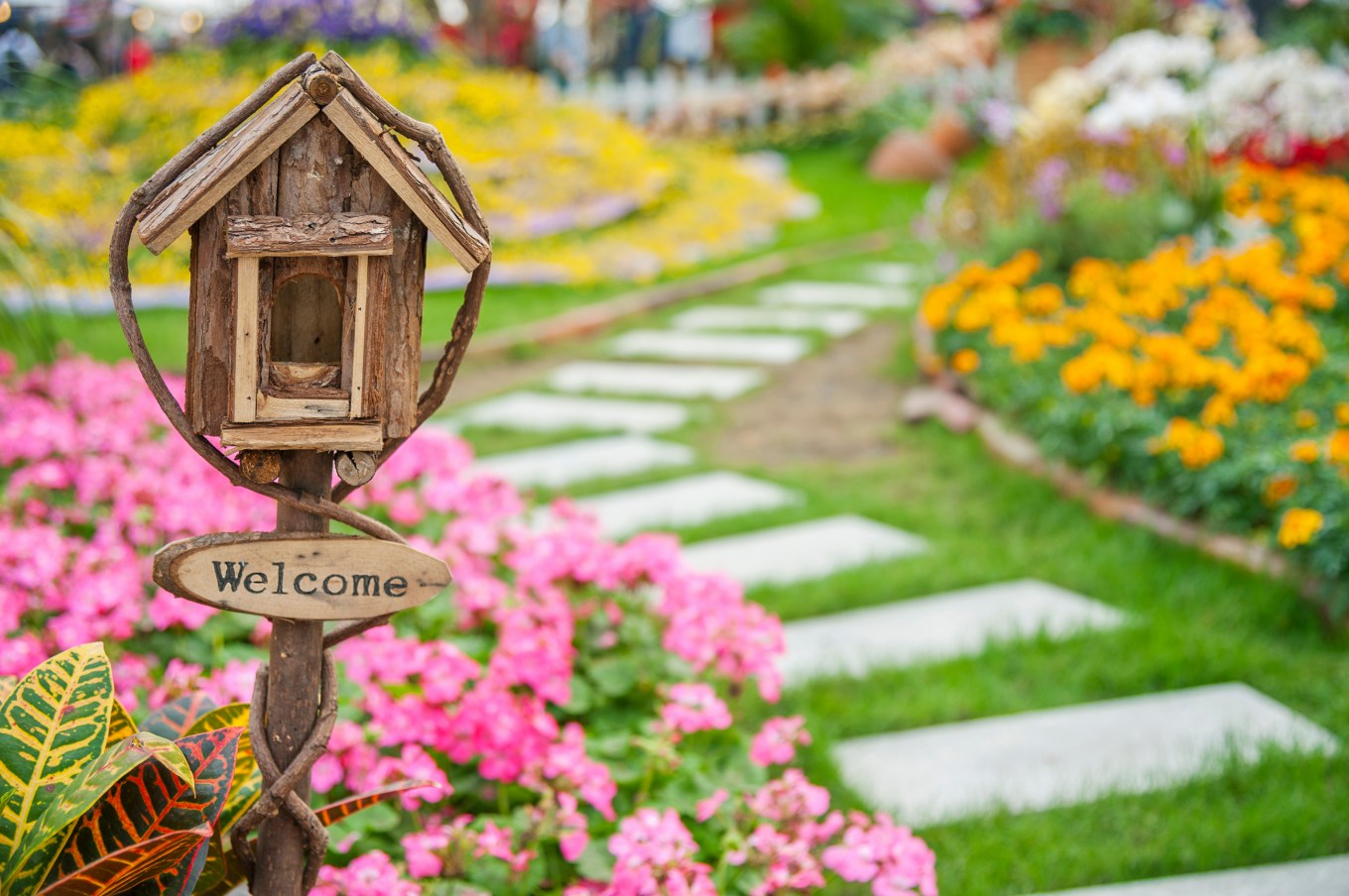 welcome yard sign on a small birdhouse in colorful landscaped garden in maintained yard of a home