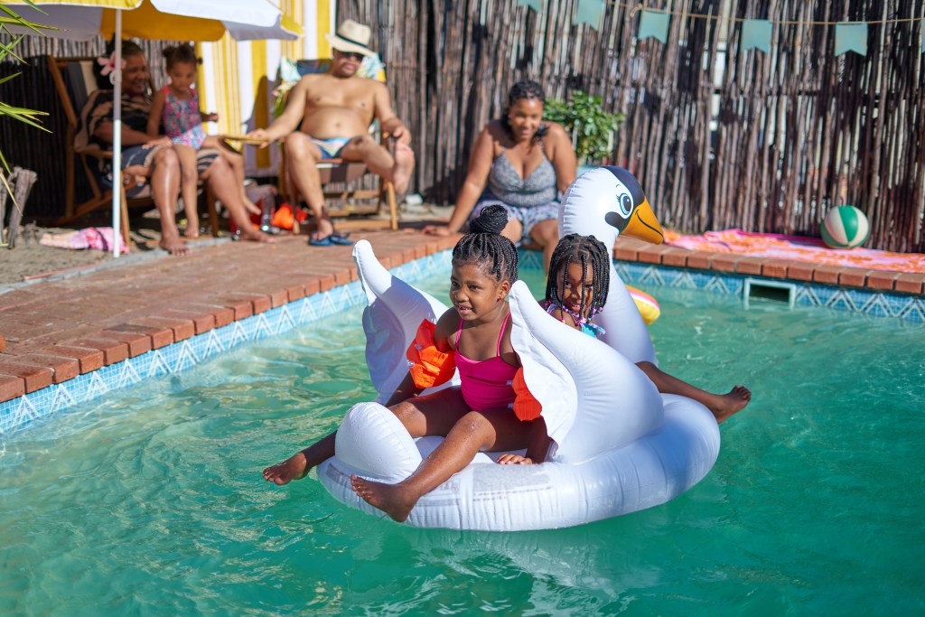 Raising the value of a home with an inground pool. Sisters playing on an inflatable swan at a family pool party.