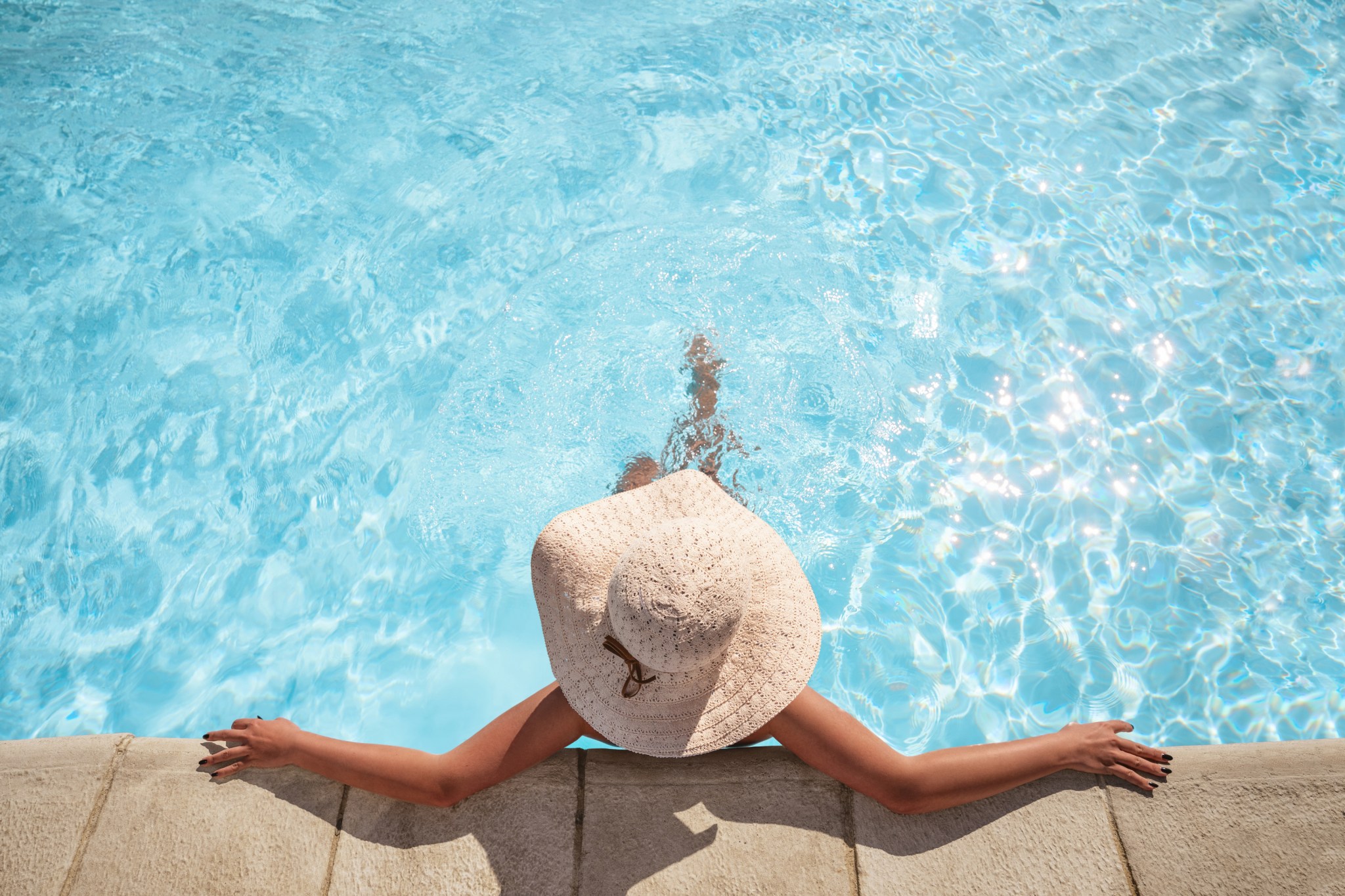 young woman wearing a hat relaxing in a clear saltwater swimming pool