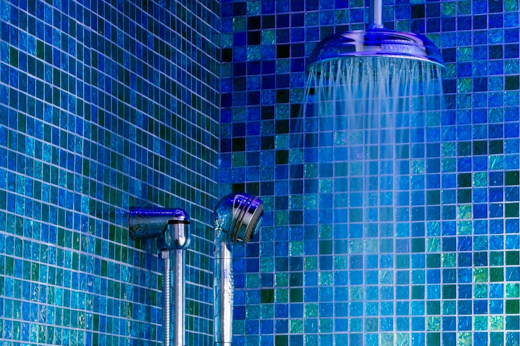 Vibrant blue and green tiles in a shower with handheld head and water pouring from a rain shower head