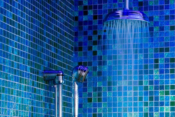 Vibrant blue and green tiles in a shower with handheld head and water pouring from a rain shower head