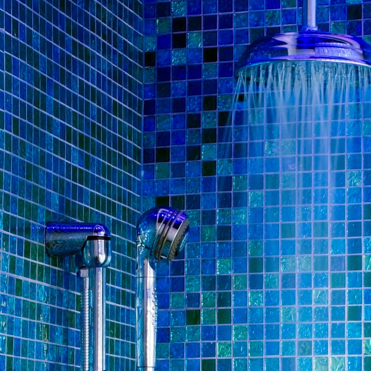 Vibrant blue and green tiles in a shower with handheld head and water pouring from a rain shower head