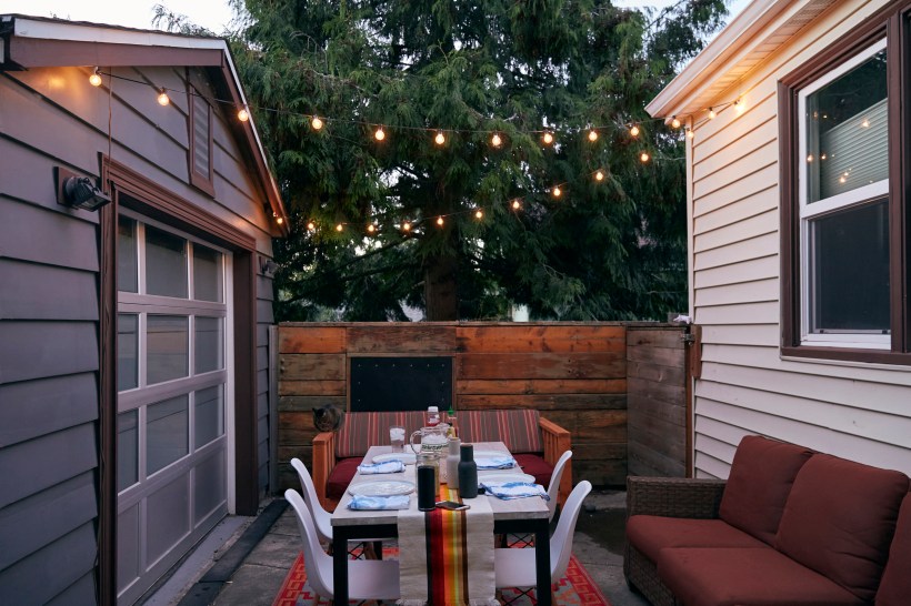 A dinner table with string lights set up overhead and a sofa, an ideal idea to make use of a backyard patio.