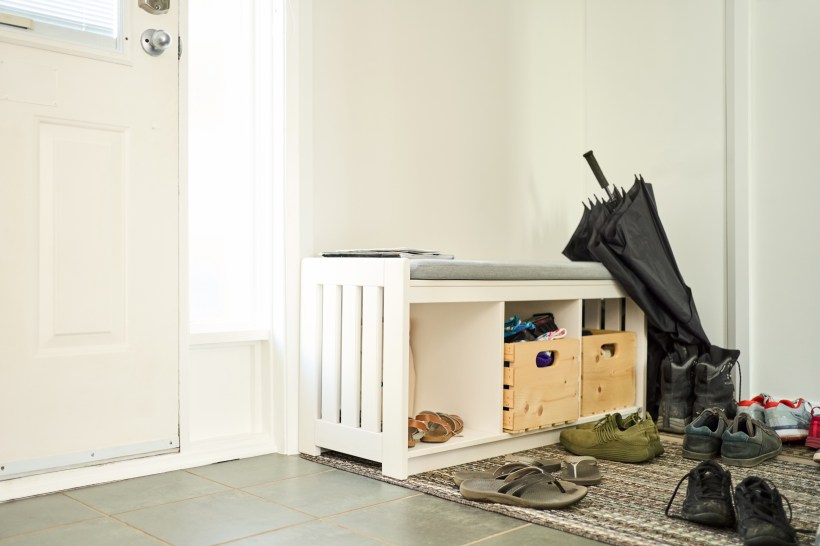 Front door of a house with a wooden bench and shoes scattered on floor.