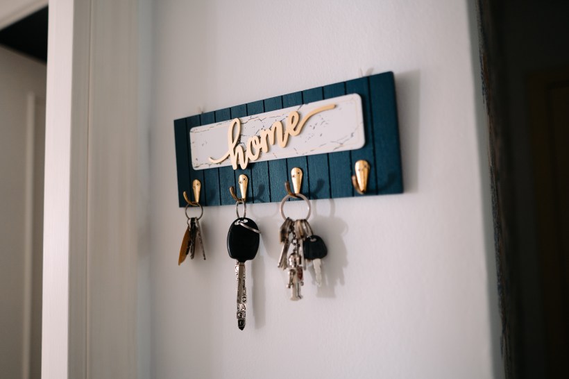 A blue wooden key hook with the golden word "home" and various keys hanging from it.